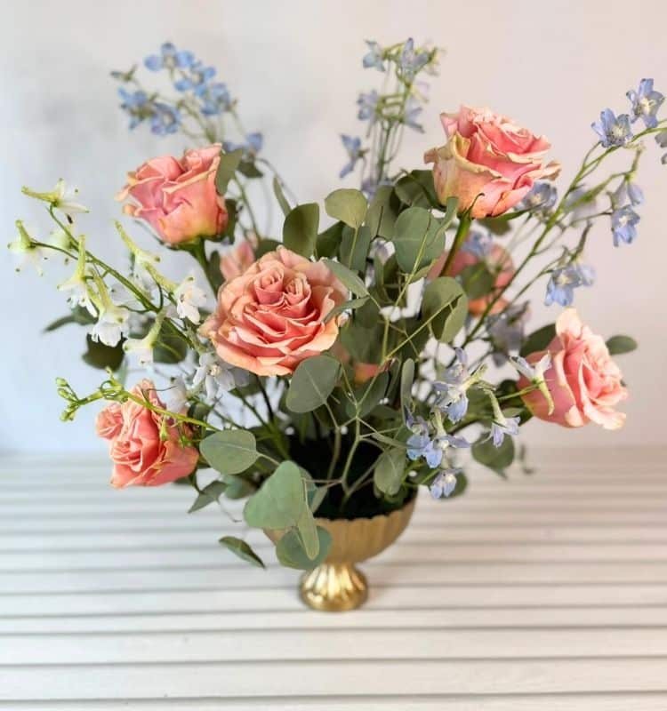 a centerpiece with eucalyptus, peach roses, and light blue delphinium.