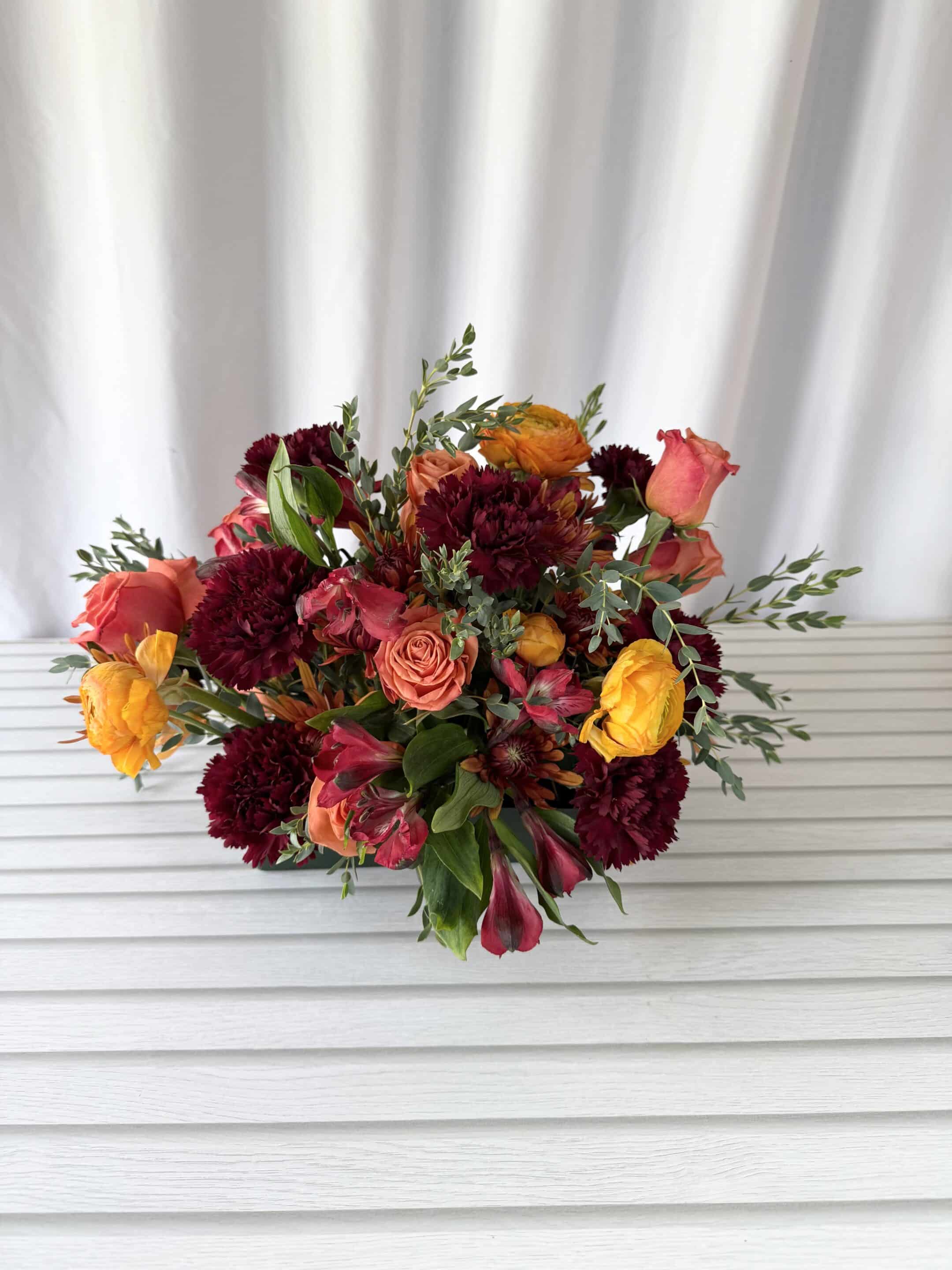 an arrangement with burgundy, bronze, and orange colored flowers.