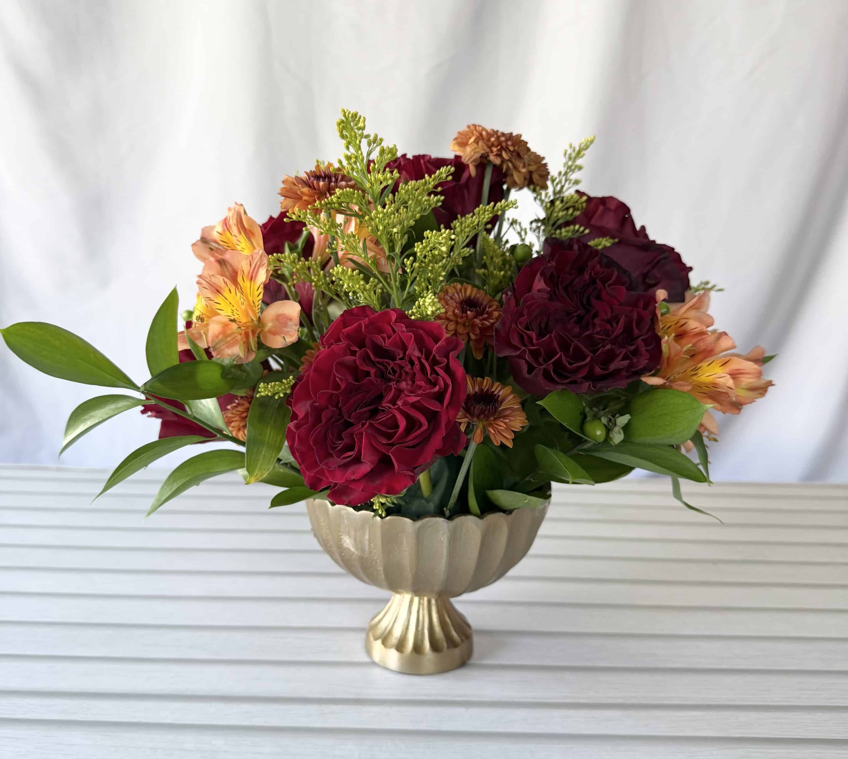 A compote arrangement with fall colored flowers.