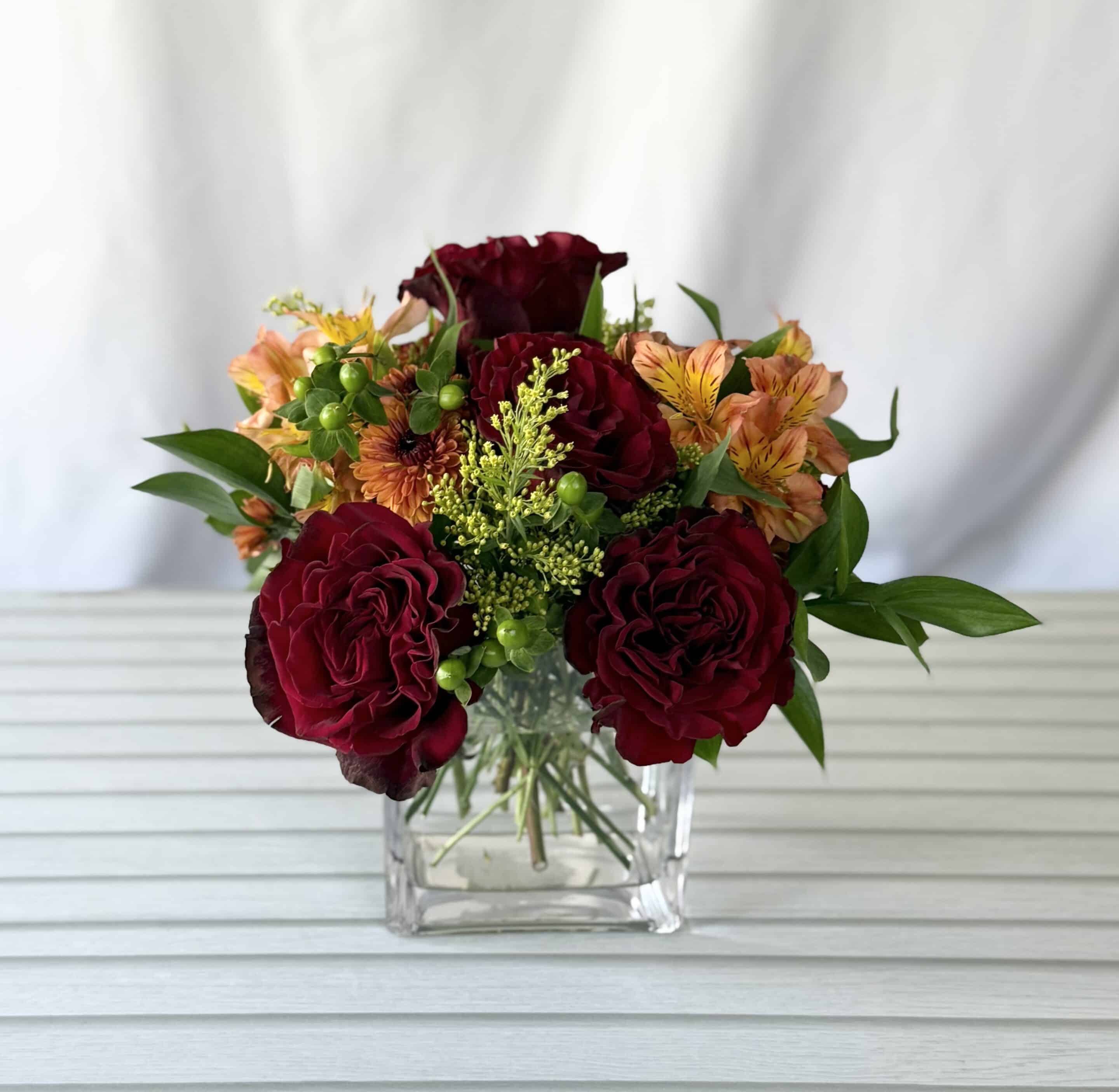 orange alstromeria and red roses in a small square glass vase