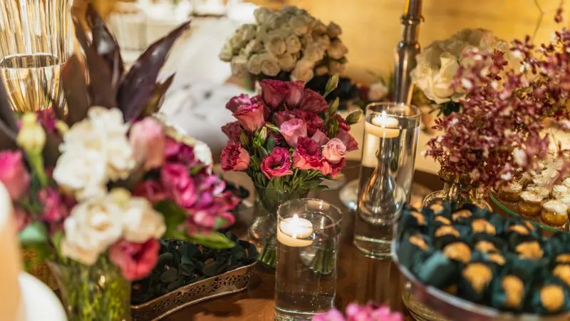 Table with pink and white flower arrangements, floating candles in glass vases, and wrapped sweets.