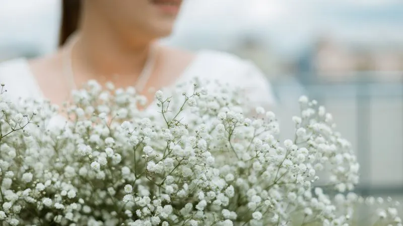 A woman in a white top and pearl necklace holds a large bunch of baby's breath.