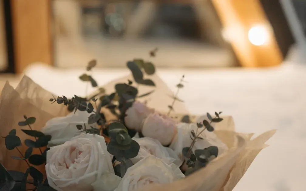 Hand-tied bouquet of white and blush roses with eucalyptus, wrapped in kraft paper