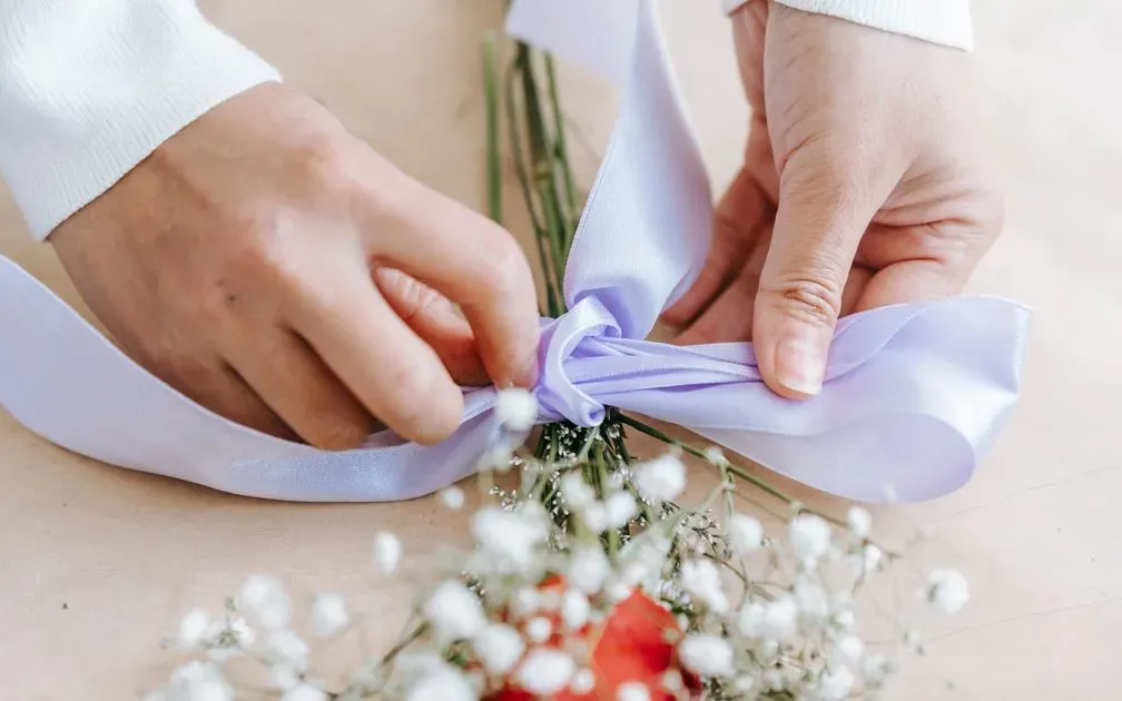 Hands tying a lavender satin ribbon around a bouquet of baby