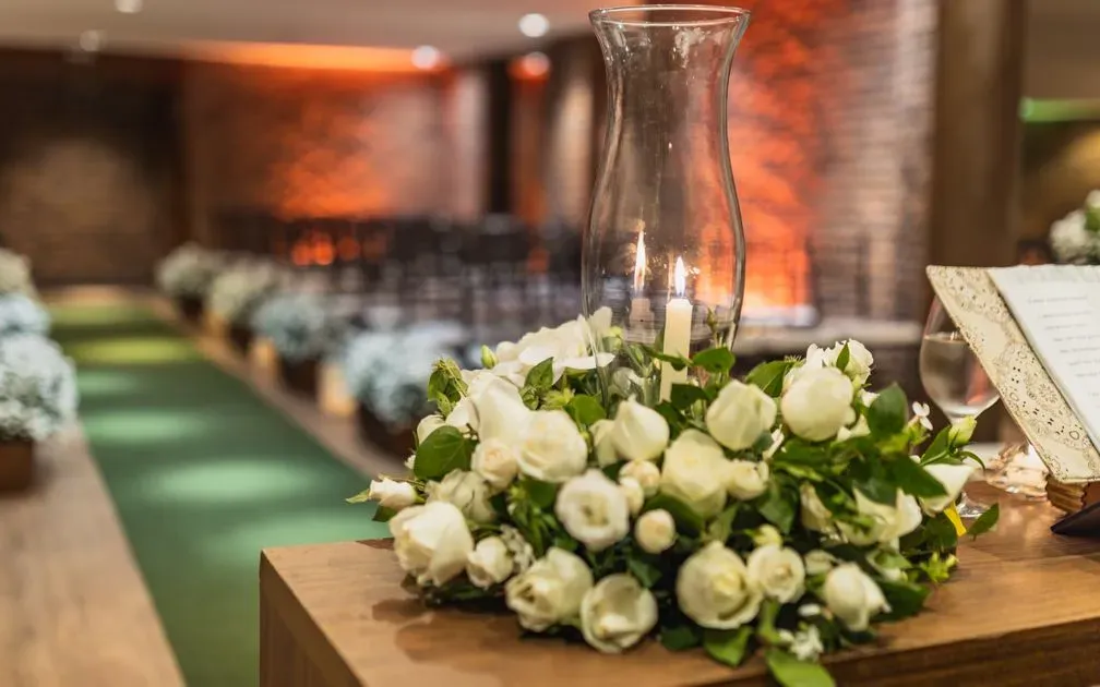 White roses and greenery around a candle in a glass hurricane at a wedding ceremony.
