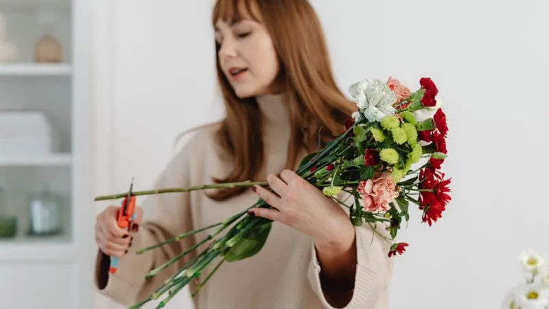 A woman trims the stems of a mixed bouquet of flowers with pruning shears.